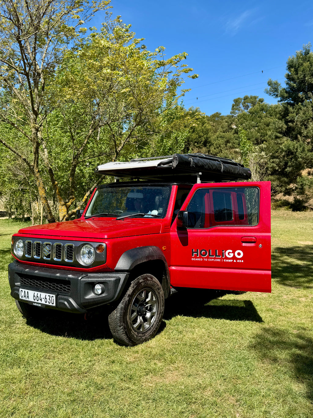 Red SUV with 'Holligo' branding parked on grass with trees in the background