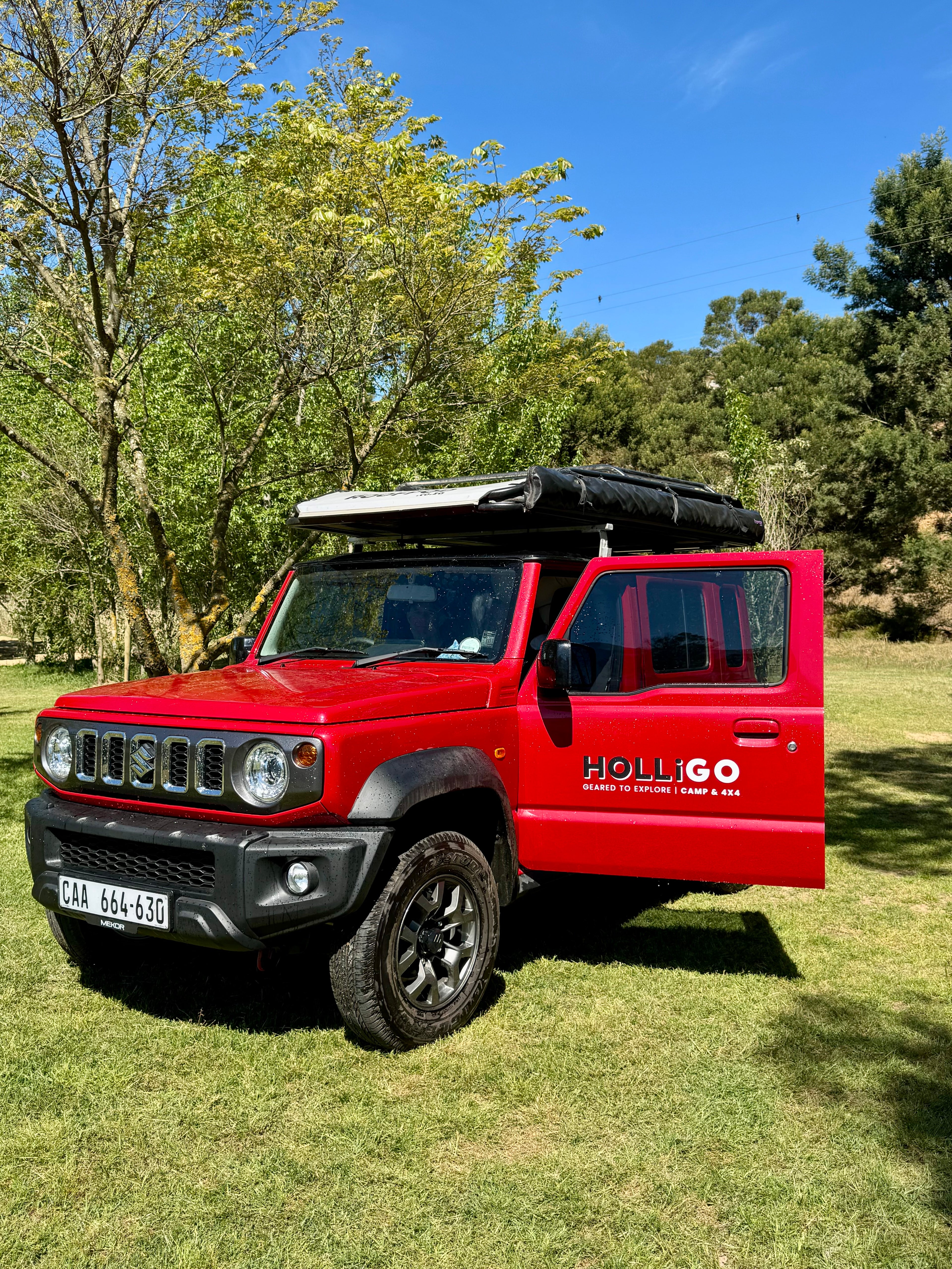 Red SUV with 'Holligo' branding parked on grass with trees in the background