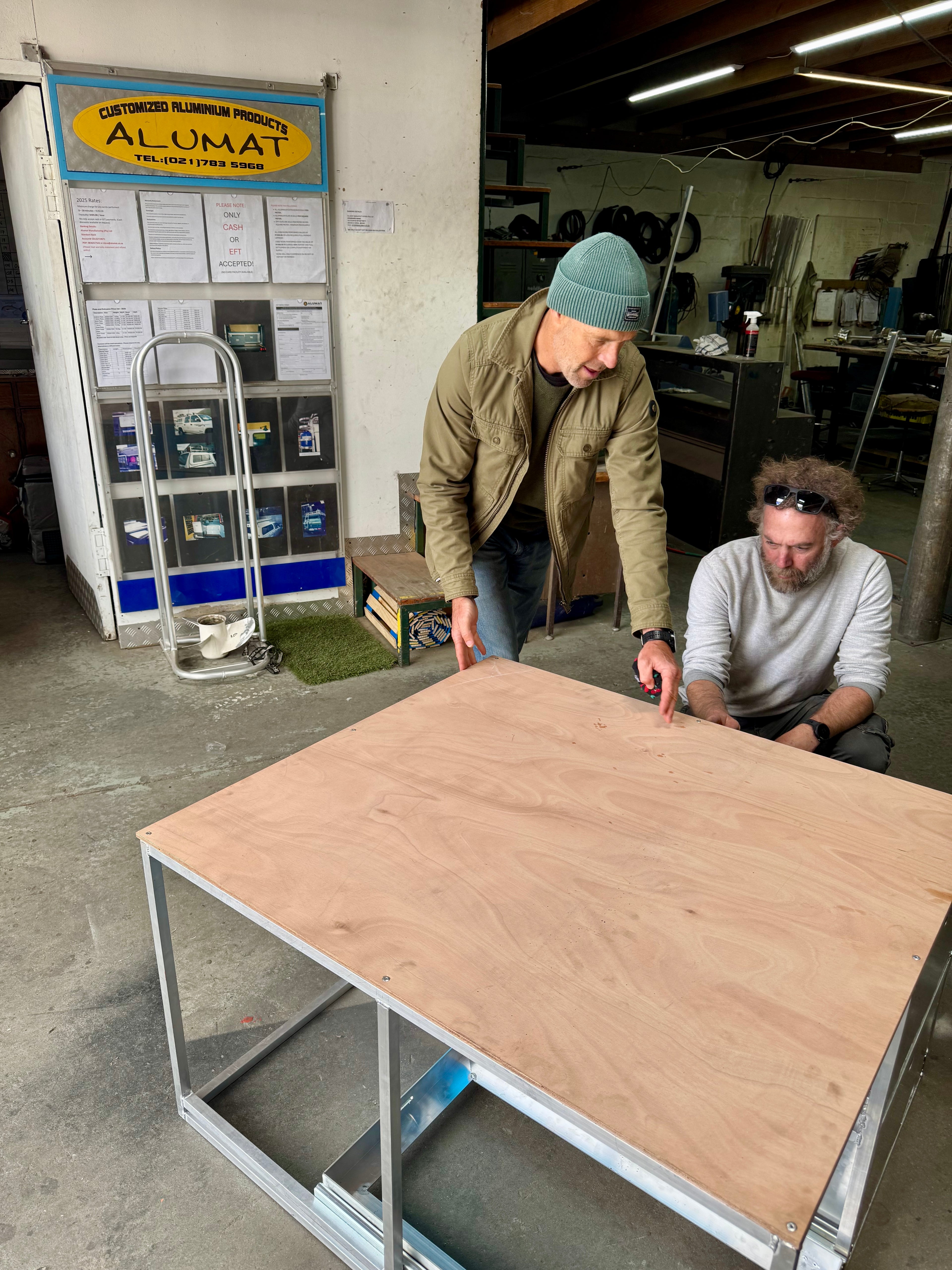 Two men inspecting a large wooden workbench in a workshop setting.
