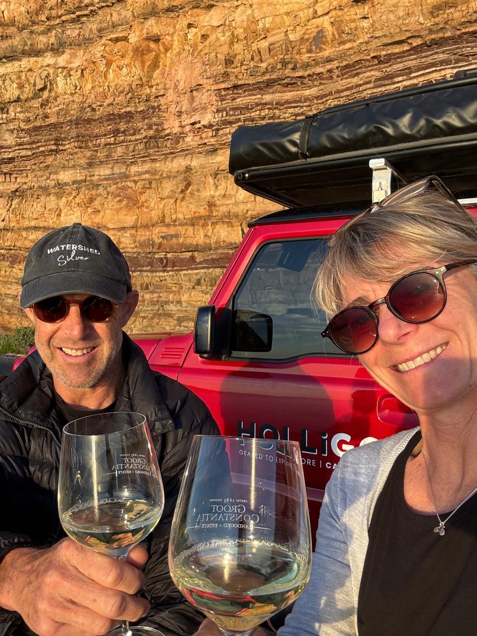 Joril and Joy smiling at camera with glass of wine with HolliGo car in the background