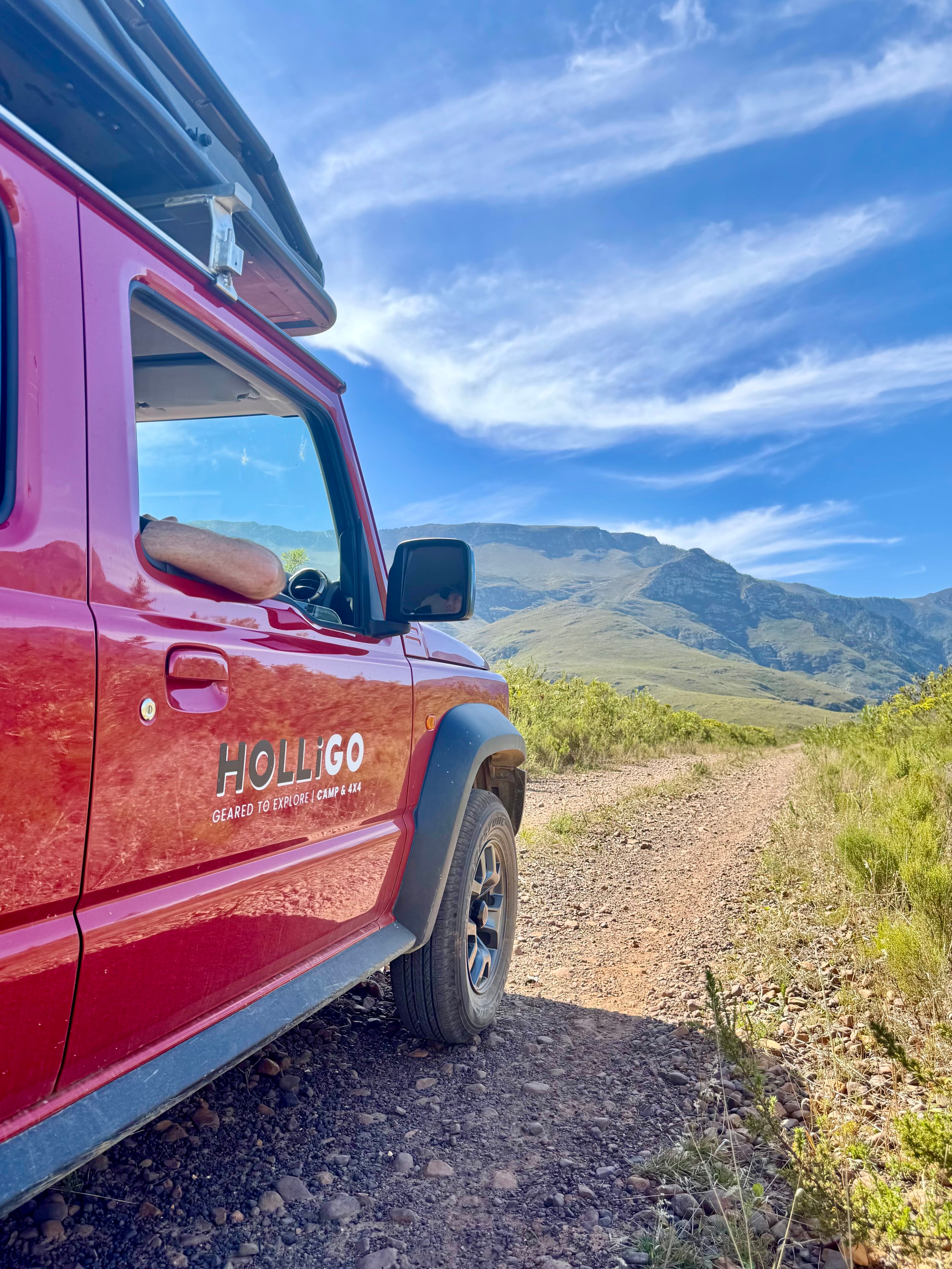 Red vehicle on a dirt road with mountains in the background