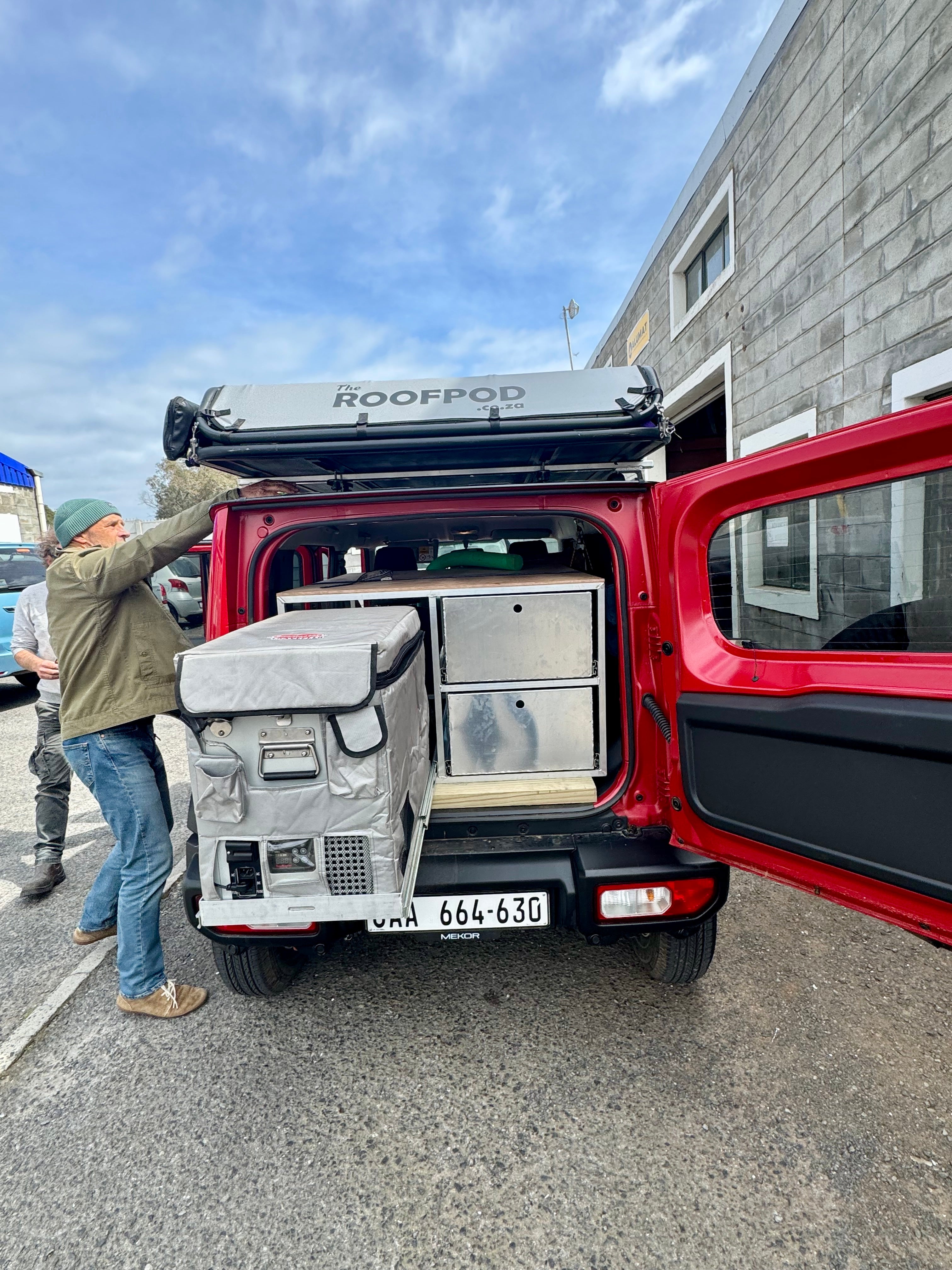 Red Suzuki with a 'ROOFPOD' on top, being loaded with equipment.