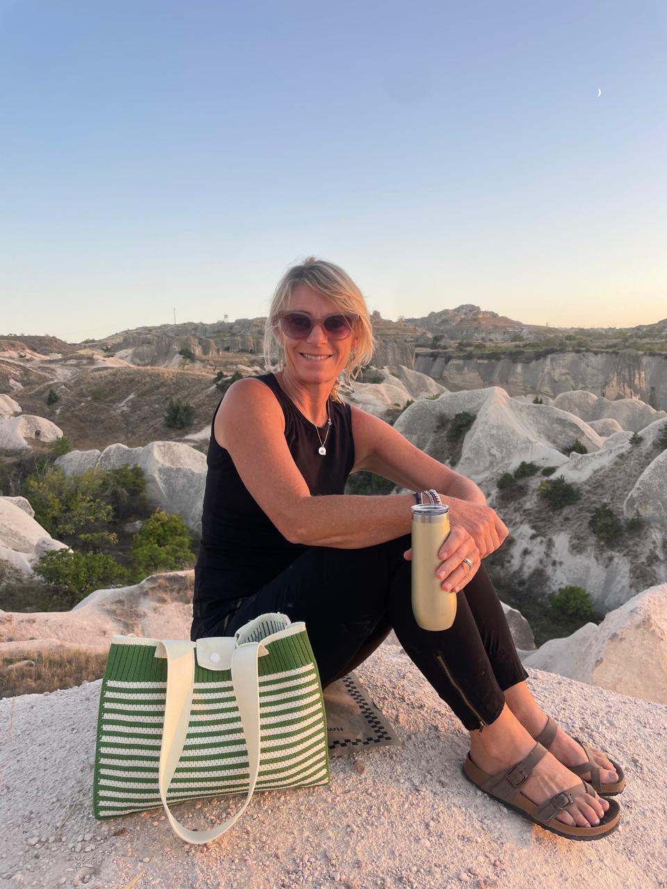 Joy Glowacki sitting on a rocky landscape with a green and white striped bag and a yellow water bottle.